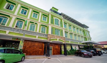 Un edificio a più piani con facciata verde, grandi porte in legno e un'area di parcheggio con diverse auto.