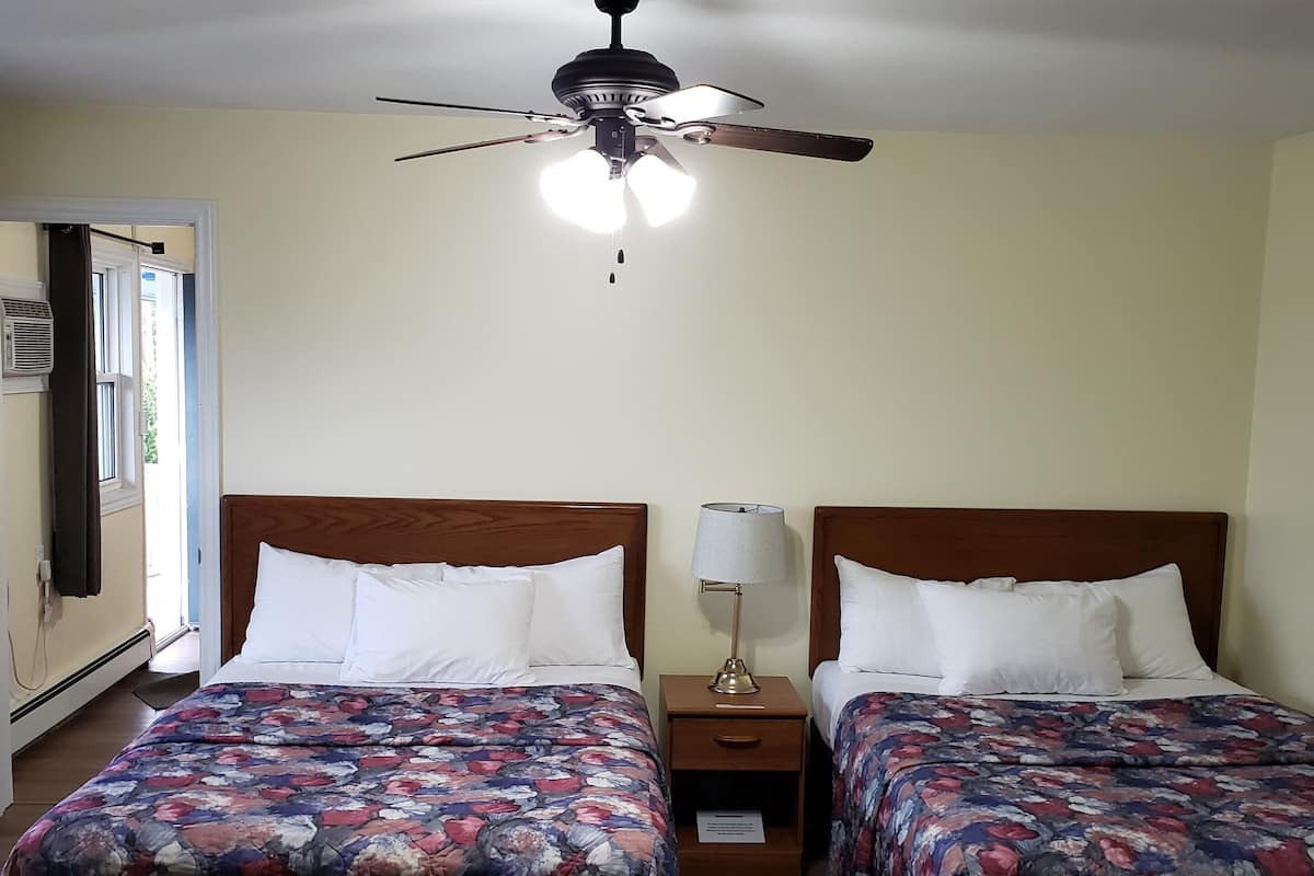 A room with two beds, a ceiling fan, and a nightstand with a lamp.