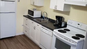 Une cuisine avec des meubles blancs, un réfrigérateur, un four à micro-ondes, un évier, une cuisinière et un ventilateur de plafond.