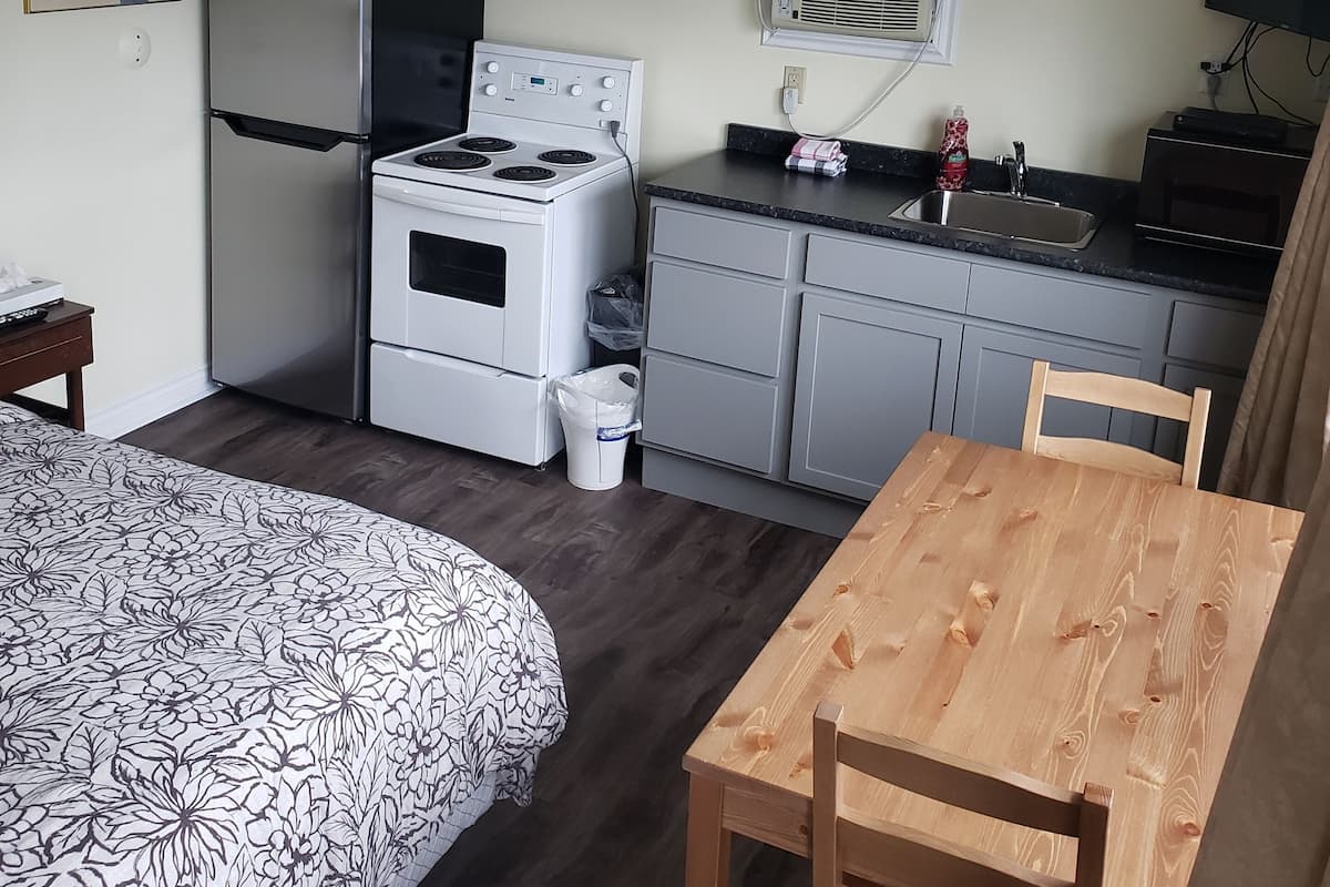 A compact kitchen with a refrigerator, stove, microwave, and sink. There is a dining table and chairs, and a ceiling fan.