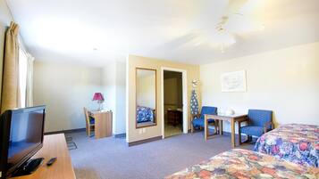 Une chambre d’hôtel comprenant un lit, un bureau avec une télévision, une chaise, une table, une lampe et un ventilateur de plafond.