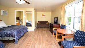 A hotel room with a bed, a sofa, a TV, a ceiling fan, and a window with curtains.
