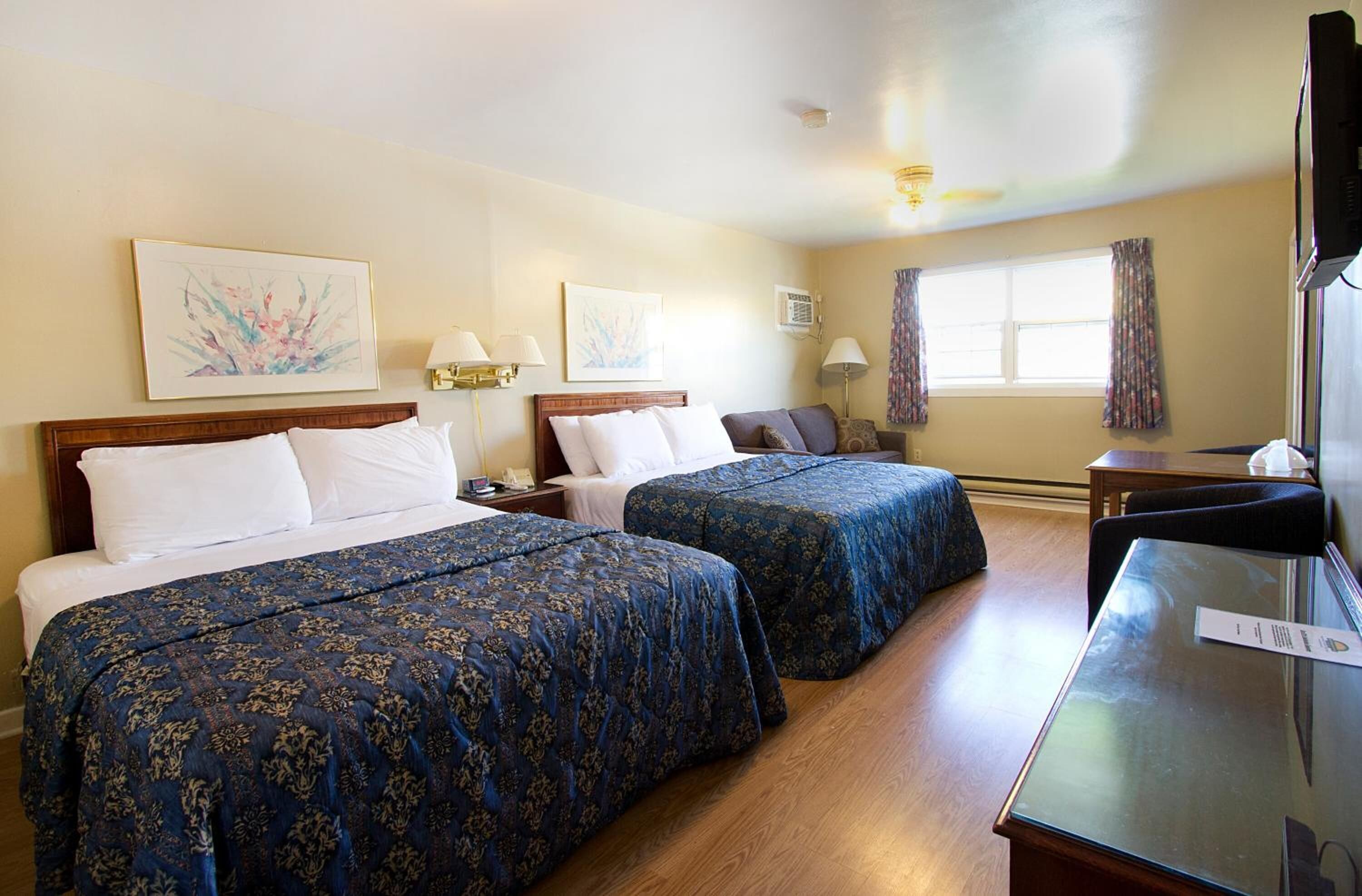 A hotel room with two beds, a desk, a TV, and artwork on the walls.