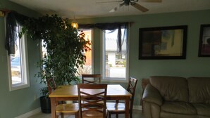 A dining area with a wooden table and chairs, a potted plant, a beige sofa, and a ceiling fan.