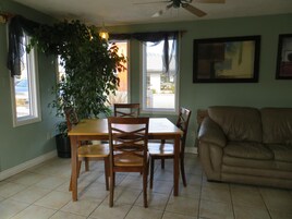 A dining area with a wooden table and chairs, a potted plant, a beige sofa, and a ceiling fan.