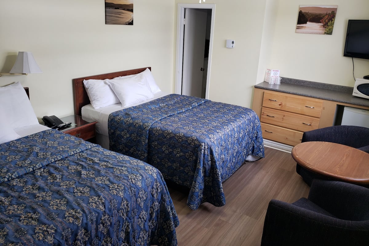 A hotel room with two beds, a desk with a flat-screen TV, a wooden dresser, and a ceiling fan.