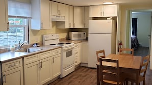 A kitchen with white cabinets, a stove, a microwave, and a dining table with chairs.
