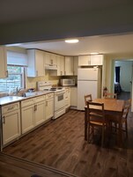 A kitchen with white cabinets, a stove, a microwave, and a dining table with chairs.