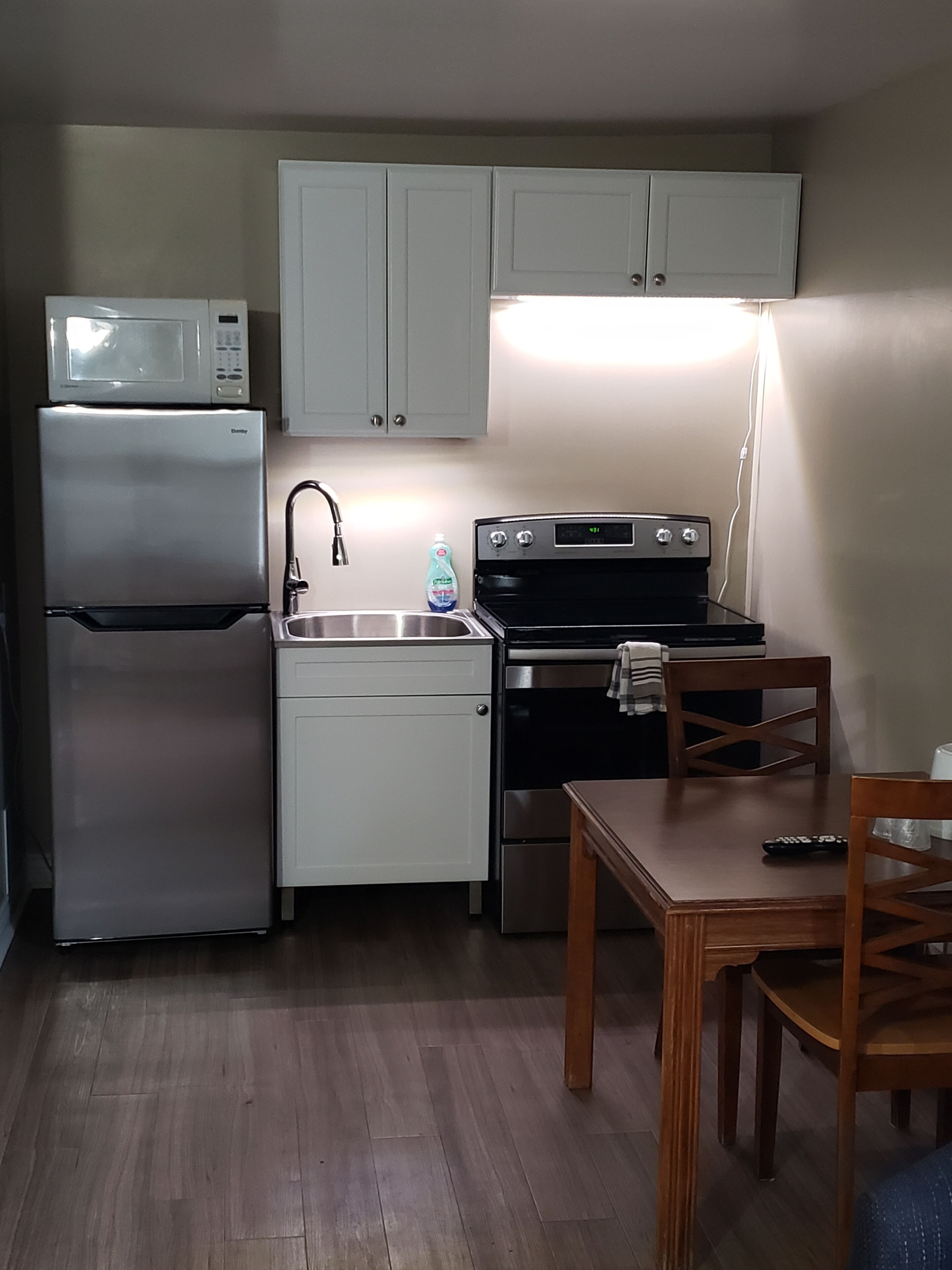 A compact kitchen with a refrigerator, microwave, sink, stove, and a dining table with chairs.