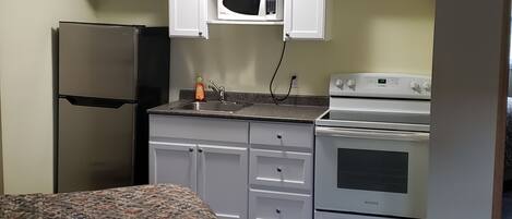 A compact kitchen with white cabinets, a microwave, a refrigerator, and an oven.