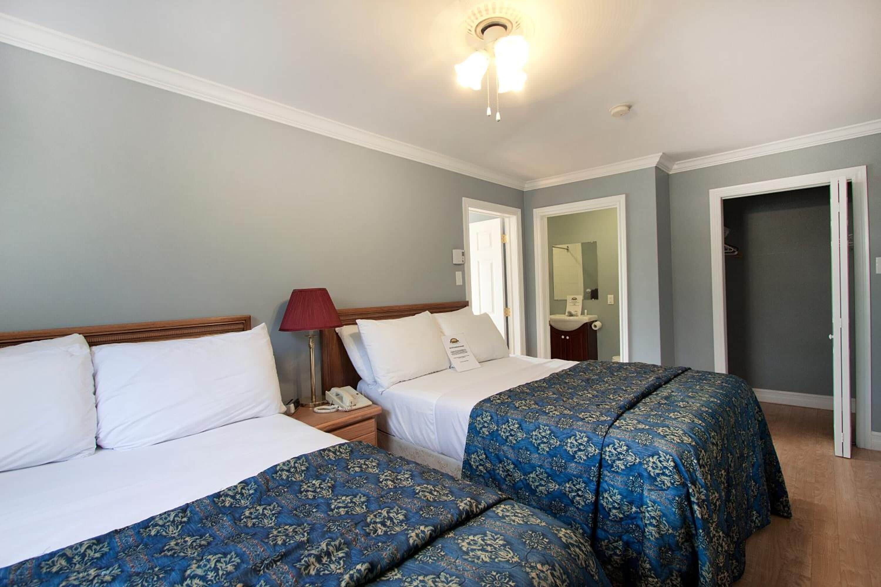 Une chambre d’hôtel avec deux lits, une table de chevet avec une lampe, un miroir et une porte donnant sur une autre pièce.