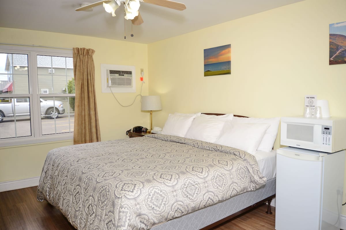 A hotel room with a bed, a nightstand, a lamp, a microwave, and a window with curtains.