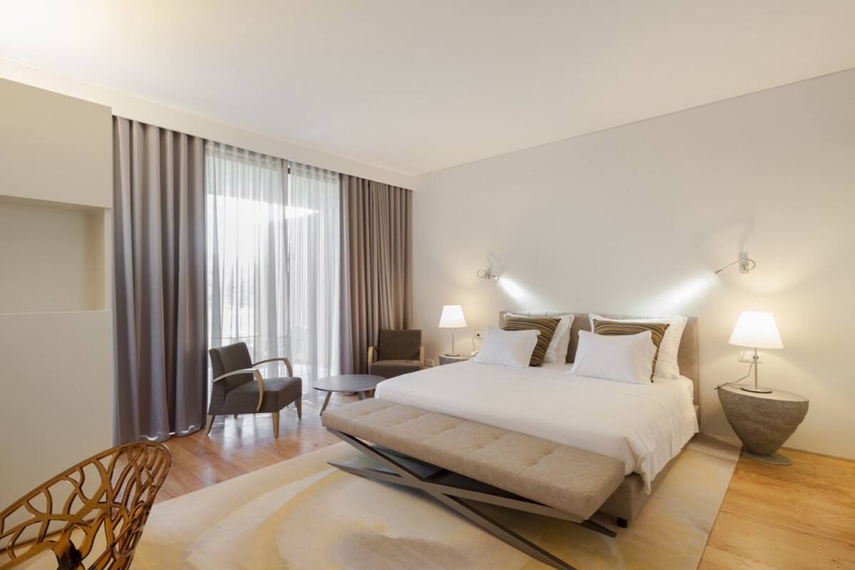 A modern hotel room with a large bed, a desk, a chair, and a sofa.