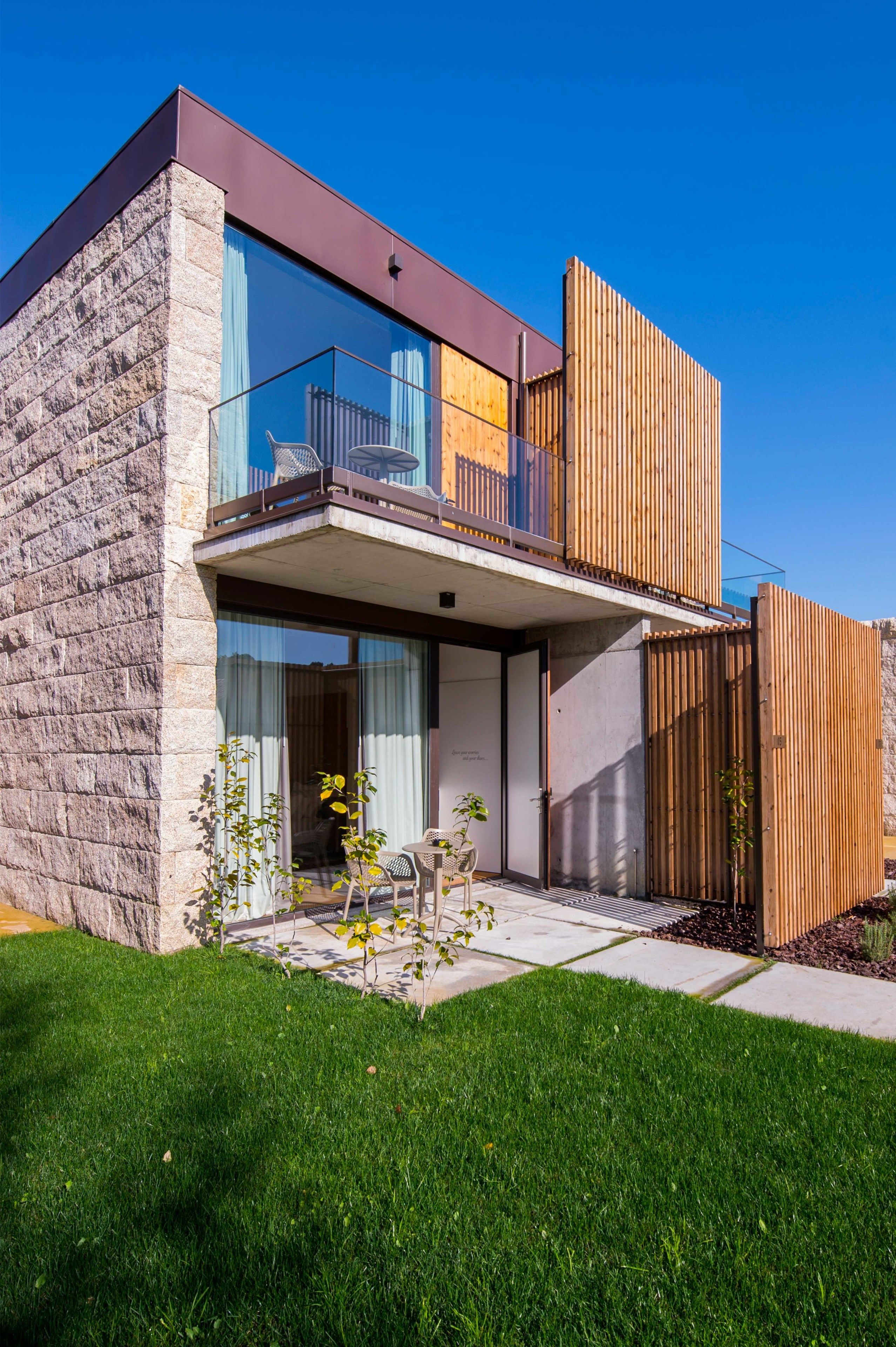 Una casa moderna de dos pisos con fachada de piedra, amplios ventanales de vidrio y una valla de madera.