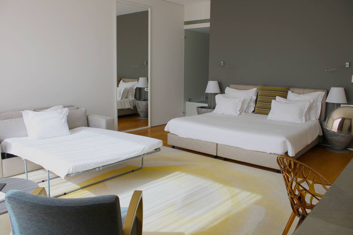 A modern hotel room with a bed, a sofa, a chair, and a small table.