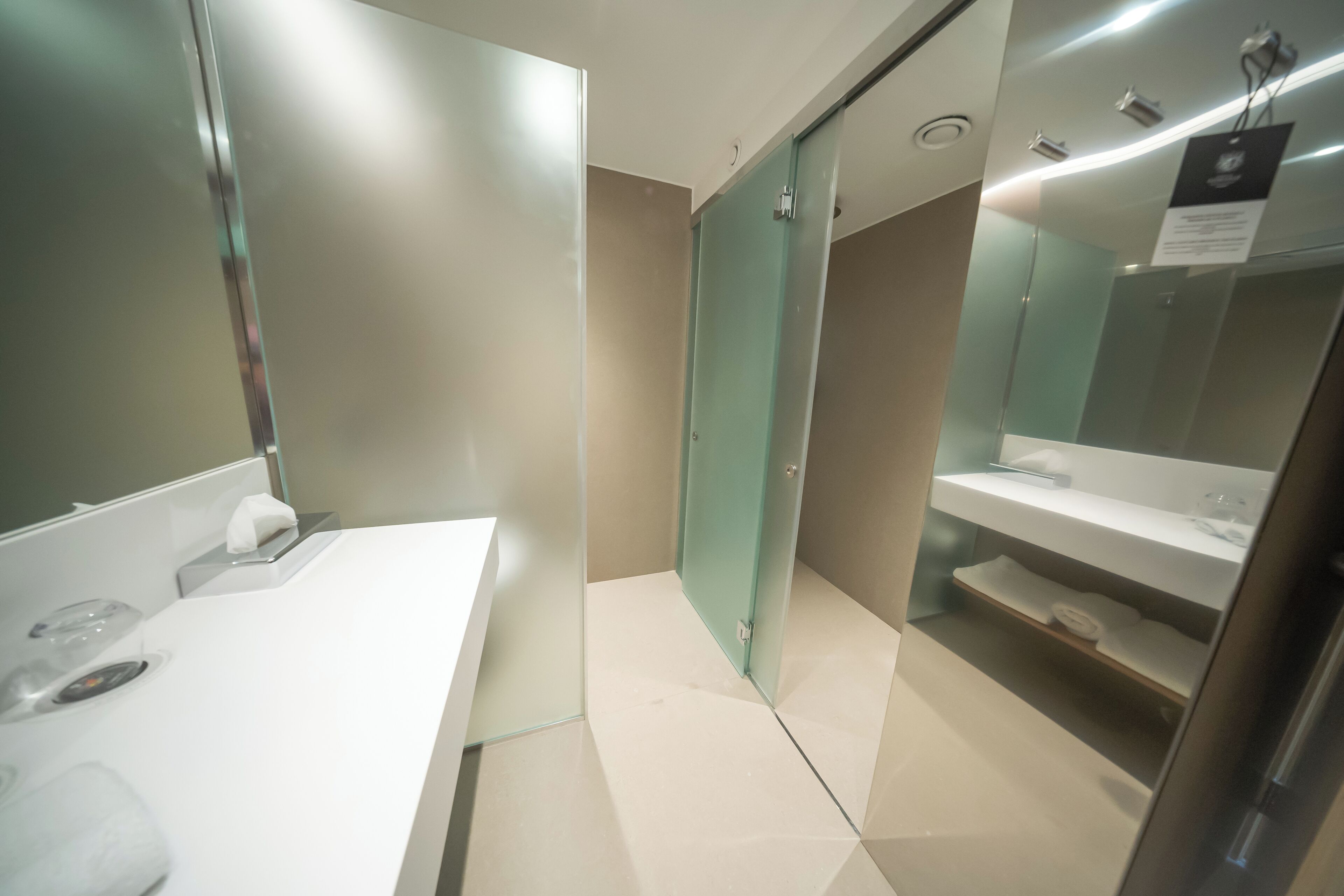 Un baño moderno con lavamanos blanco, cabina de ducha con paredes de vidrio y un espejo.