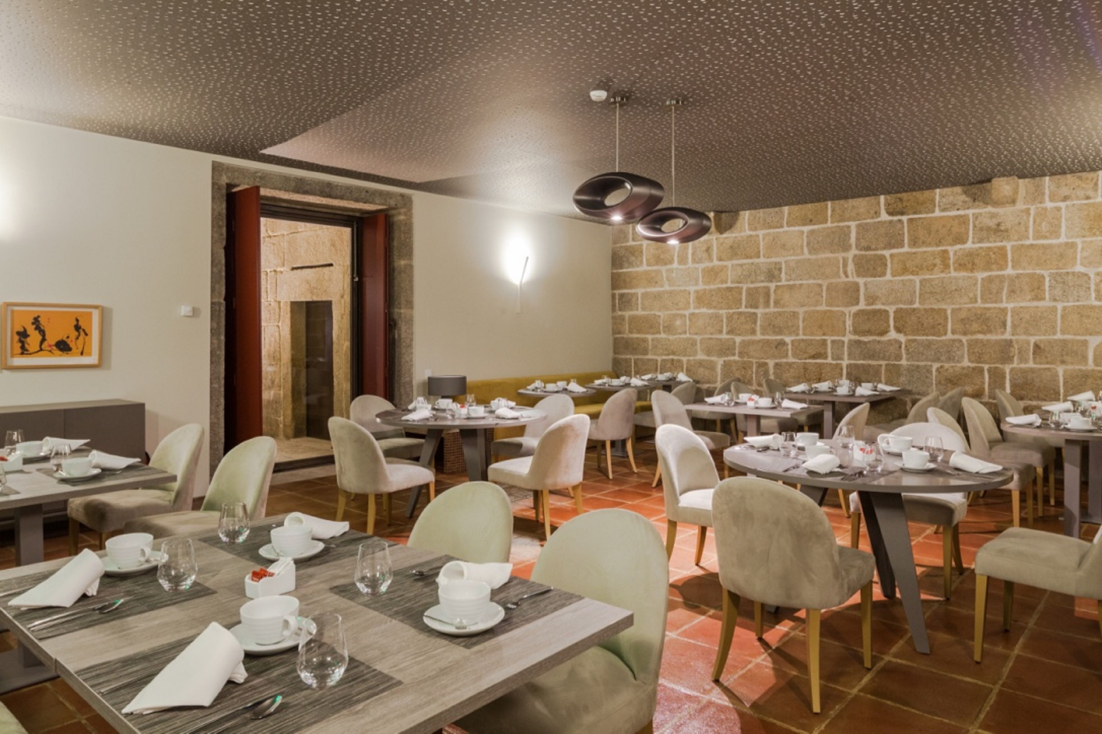 A dining area with multiple tables set for meals, chairs, and a stone wall in the background.