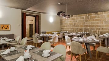 A dining area with multiple tables set for meals, chairs, and a stone wall in the background.