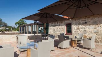 An outdoor patio with stone walls, glass tables, and white chairs.