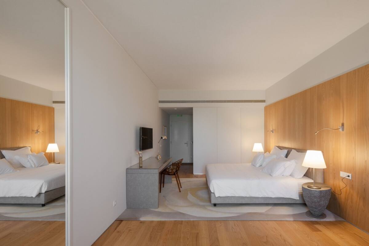 A modern hotel room with two beds, a desk, and a mirror.