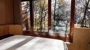 A bedroom with a large window, wooden walls, and a bed.