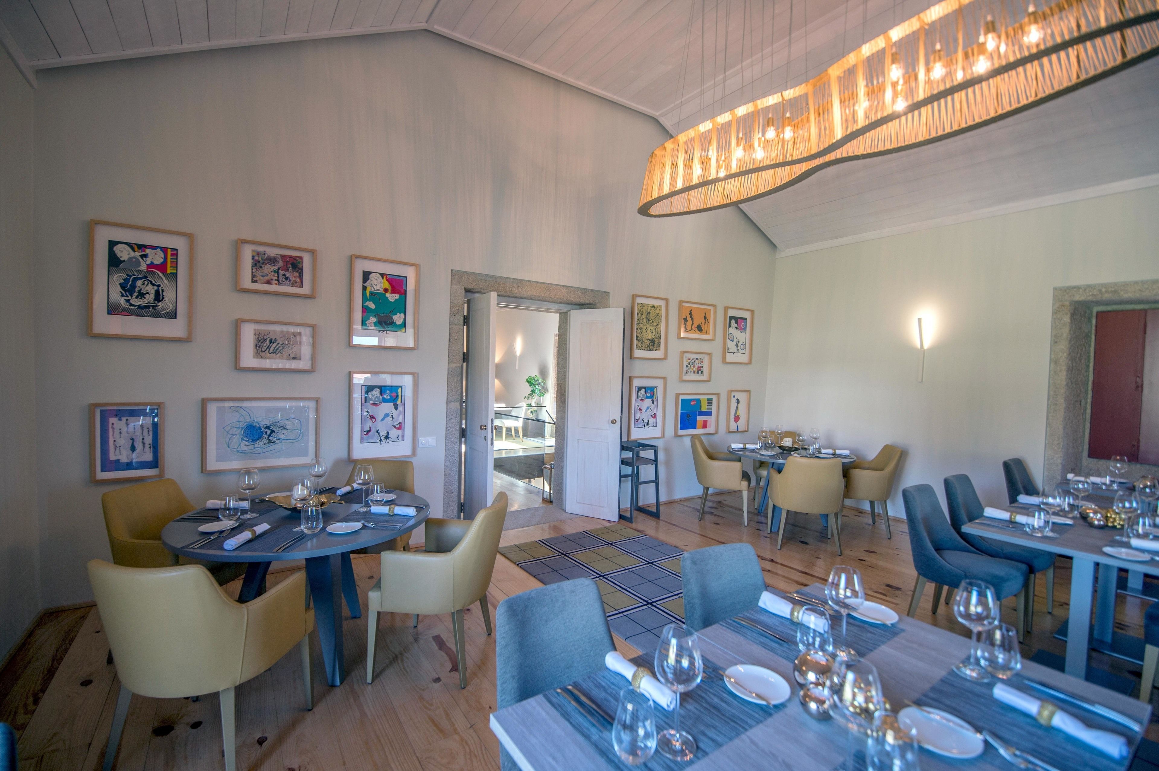 A dining area with tables set for service, framed artwork on the walls, and a modern chandelier.