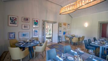 A dining area with tables set for service, framed artwork on the walls, and a modern chandelier.