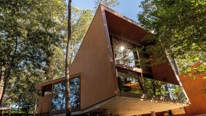 Eine moderne Holzhütte mit großen Fenstern, erhöhter Lage und Blick auf den umliegenden Wald.