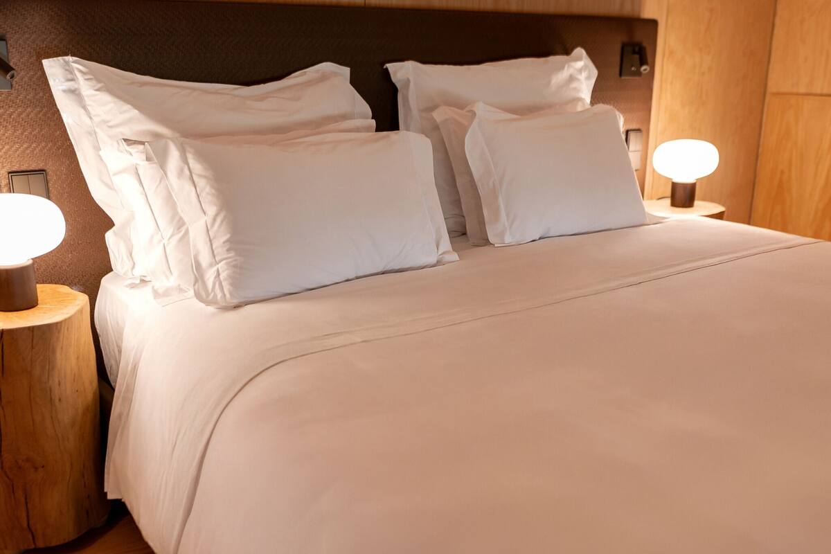A neatly made bed with white bedding, two bedside lamps, and a wooden headboard.