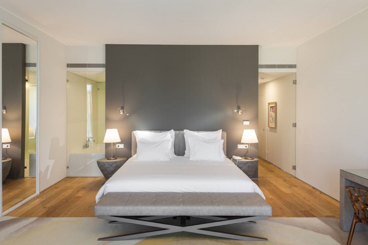 A modern bedroom with a large bed, bedside lamps, a mirror, and a wooden floor.