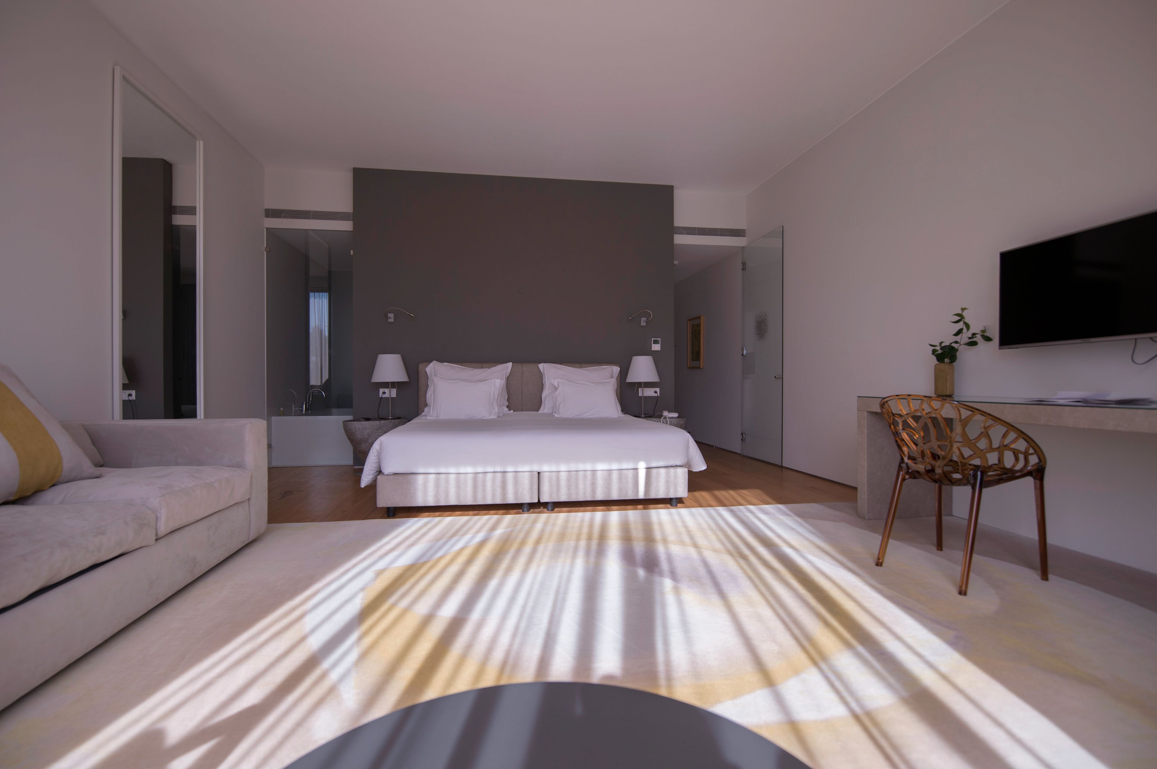 A modern hotel room with a large bed, a sofa, a TV, and a small table.