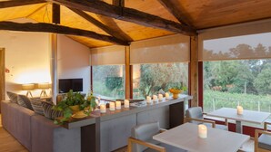 Ein modernes Interieur mit Holzbalkendecke, einer Couch, einem Essbereich und großen Fenstern mit Blick auf Grünflächen.