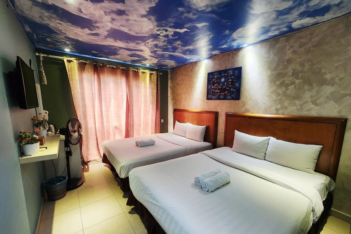 A hotel room with two beds, a ceiling mural, a painting, and a TV on the wall.
