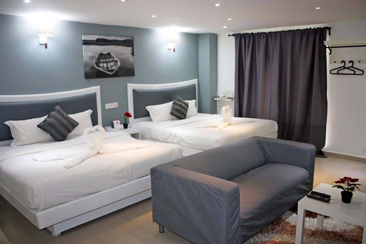 A hotel room with two beds, a grey sofa, a painting of a boat, and a coat rack.