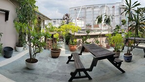 Un patio al aire libre con varias mesas y bancos de madera, rodeado de plantas en macetas y vistas a la ciudad.