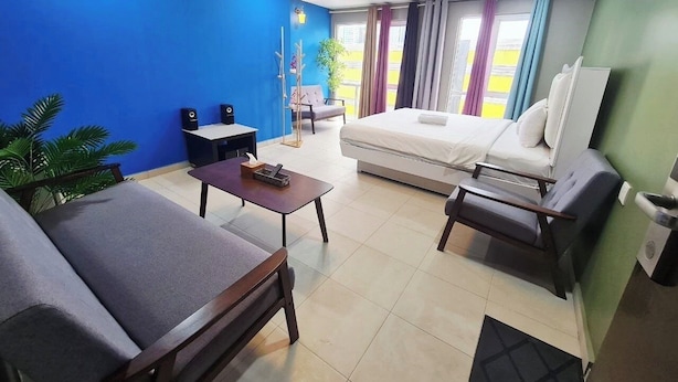 Habitación de hotel con cama, dos sofás, una mesita, televisor y ventana con cortinas.