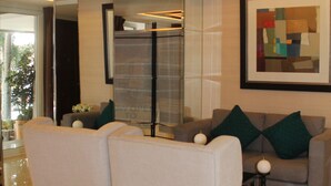 A modern living room with a sofa, chairs, and a coffee table. There is a framed abstract painting on the wall and a potted plant on the windowsill. - Stradella Hotel (Pasig)