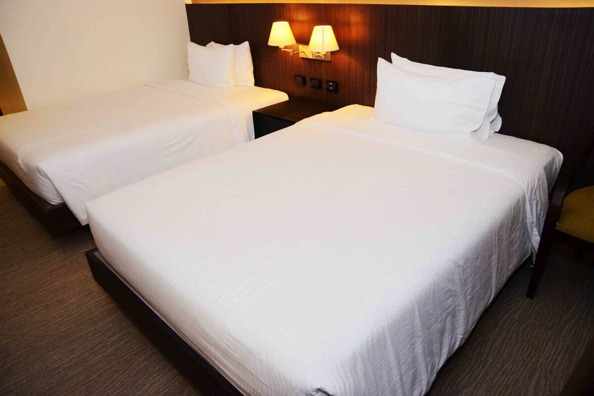A hotel room with two single beds, a wooden headboard, and a nightstand with two lamps.