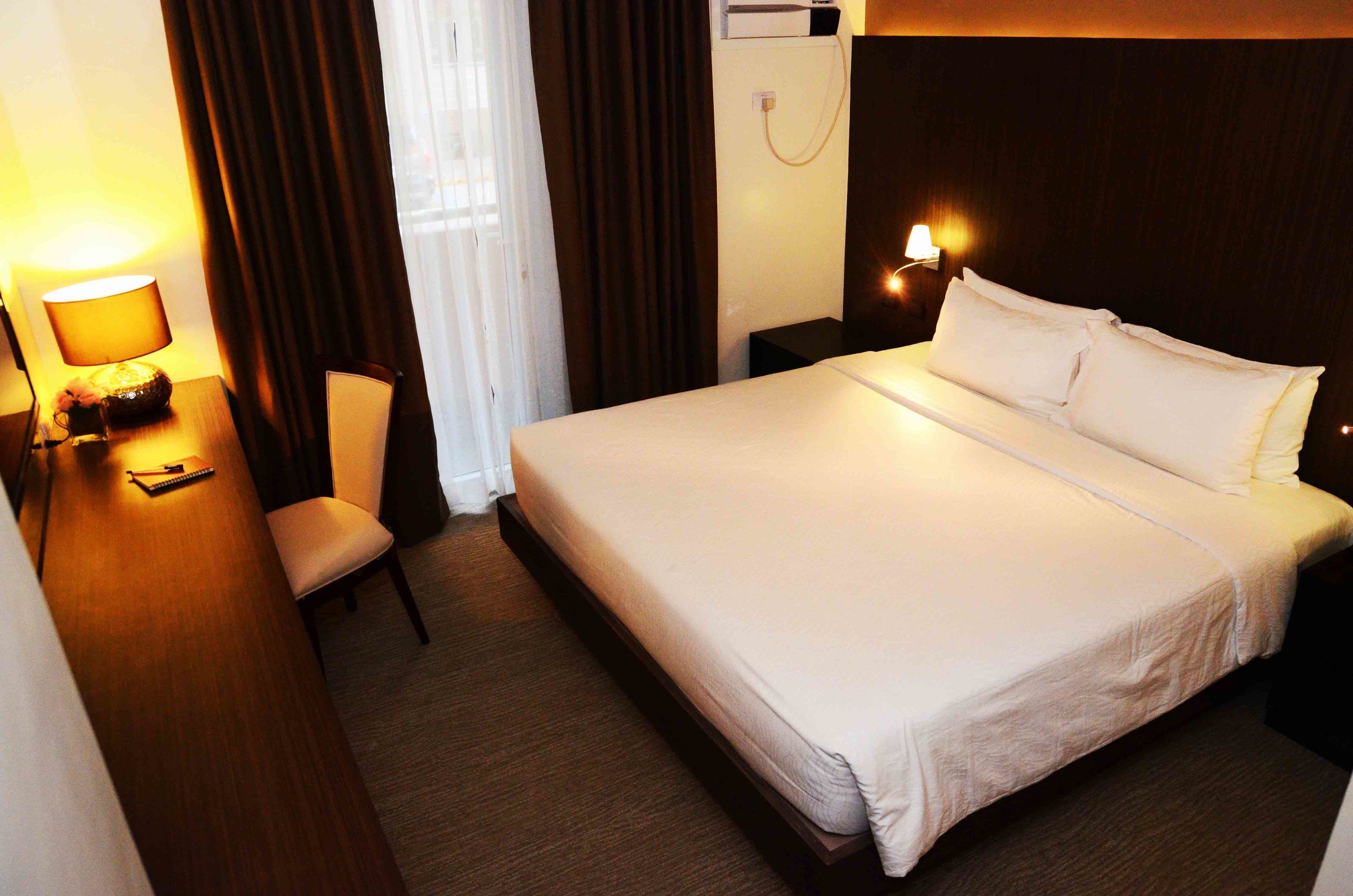Une chambre d’hôtel avec un grand lit, un bureau avec une lampe, une chaise et une table de chevet avec une lampe.