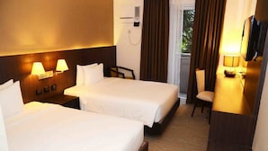 A hotel room with two beds, a desk, a chair, a TV, and a window with curtains. - Stradella Hotel (Pasig)