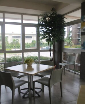 A dining area with a table and chairs, large windows, and a potted plant. - Stradella Hotel (Pasig)