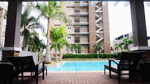 A pool area with lounge chairs, palm trees, and a multi-story building in the background. - Stradella Hotel (Pasig)