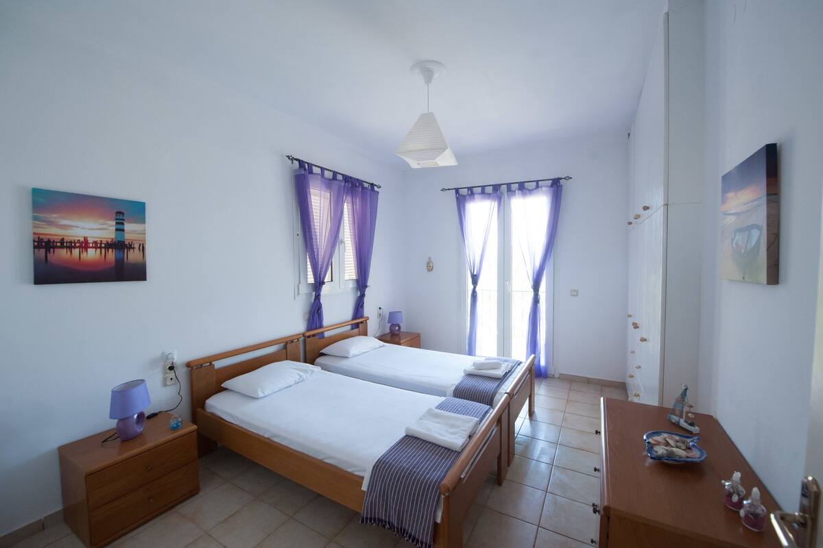 A double bed with a wooden frame, two bedside tables, a night lamp, and a painting of a sunset scene.