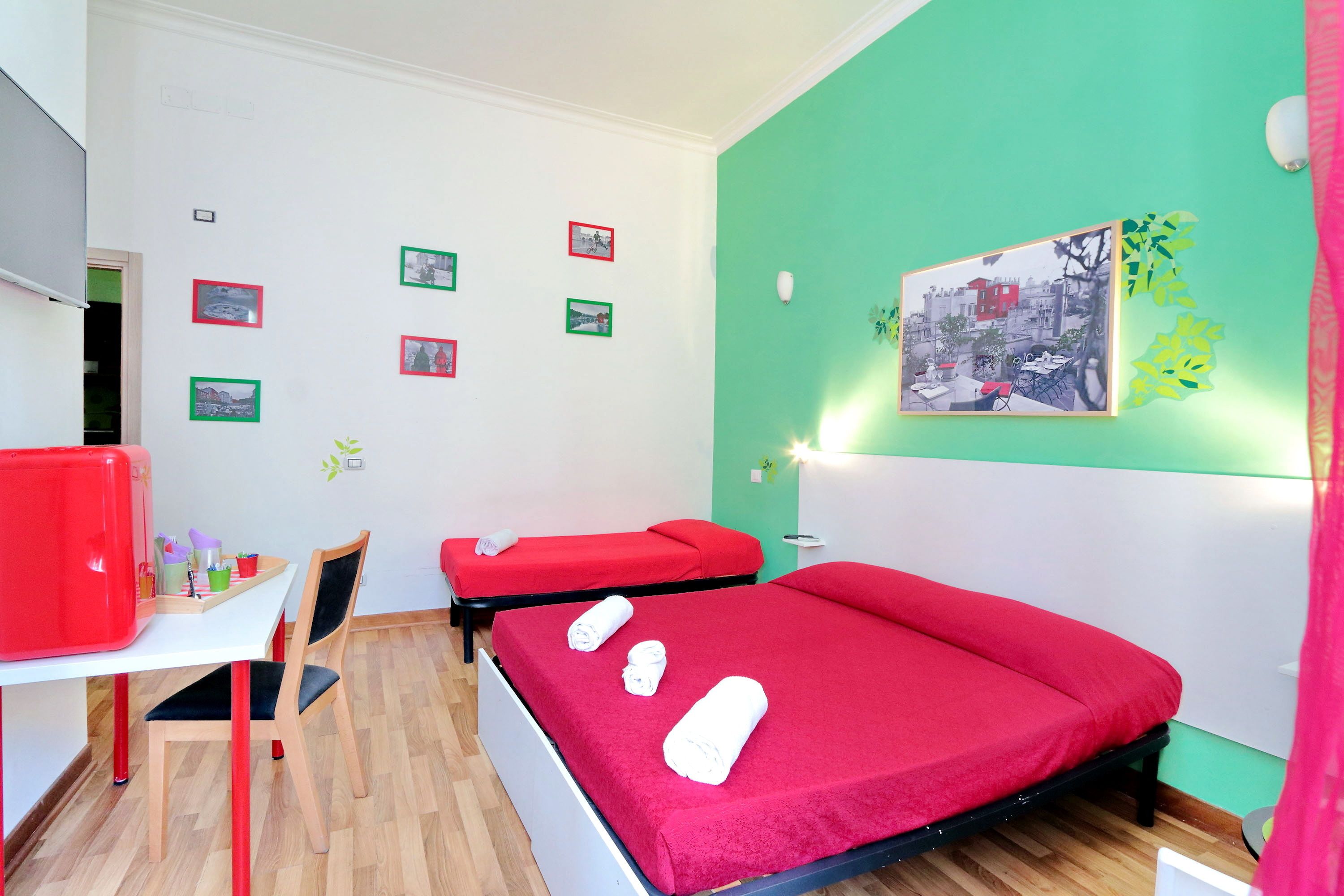 A room with two beds, a desk, and a chair. There are pictures on the wall and a red chair.