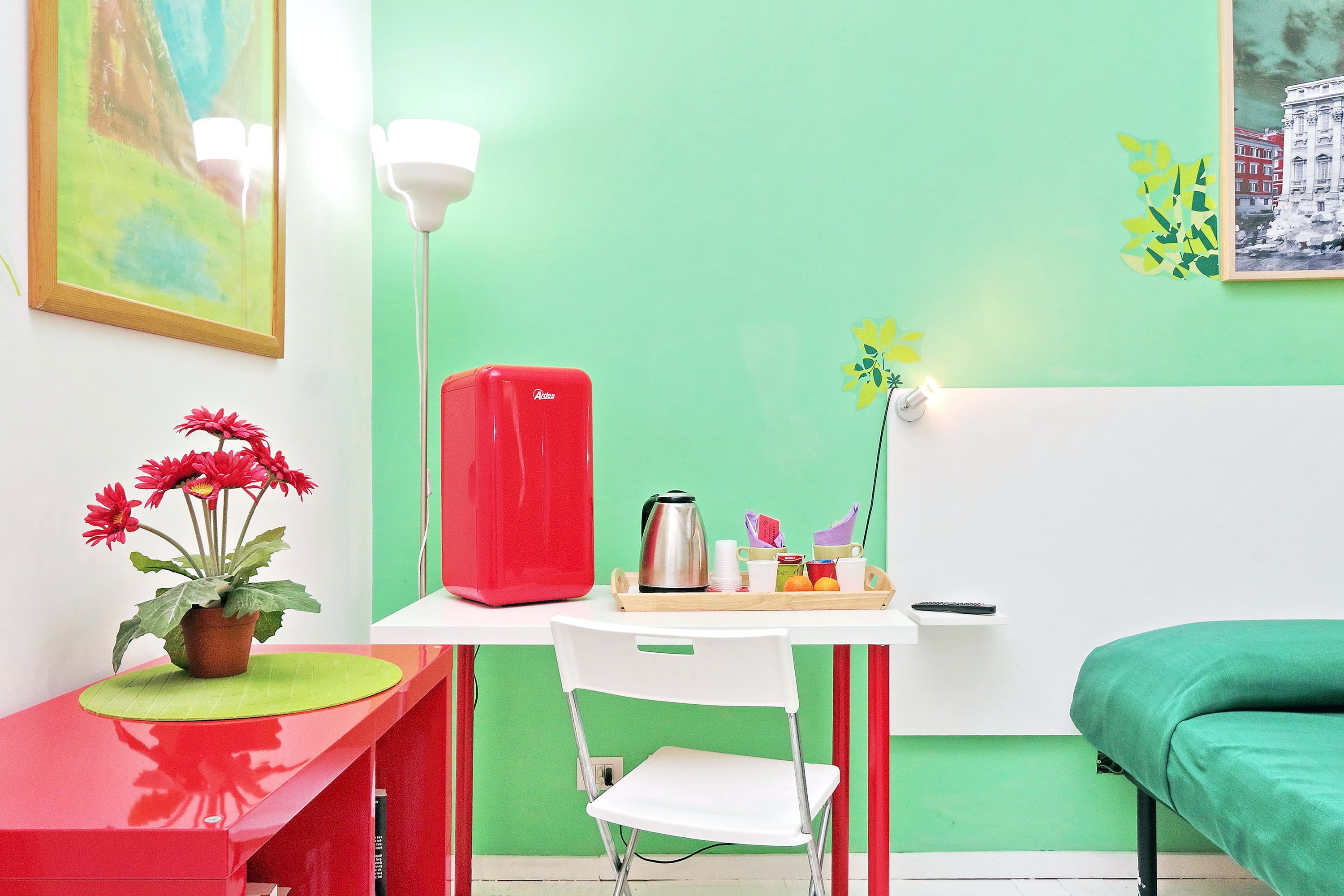 A room with a green wall, a red refrigerator, a white chair, and a green bed.