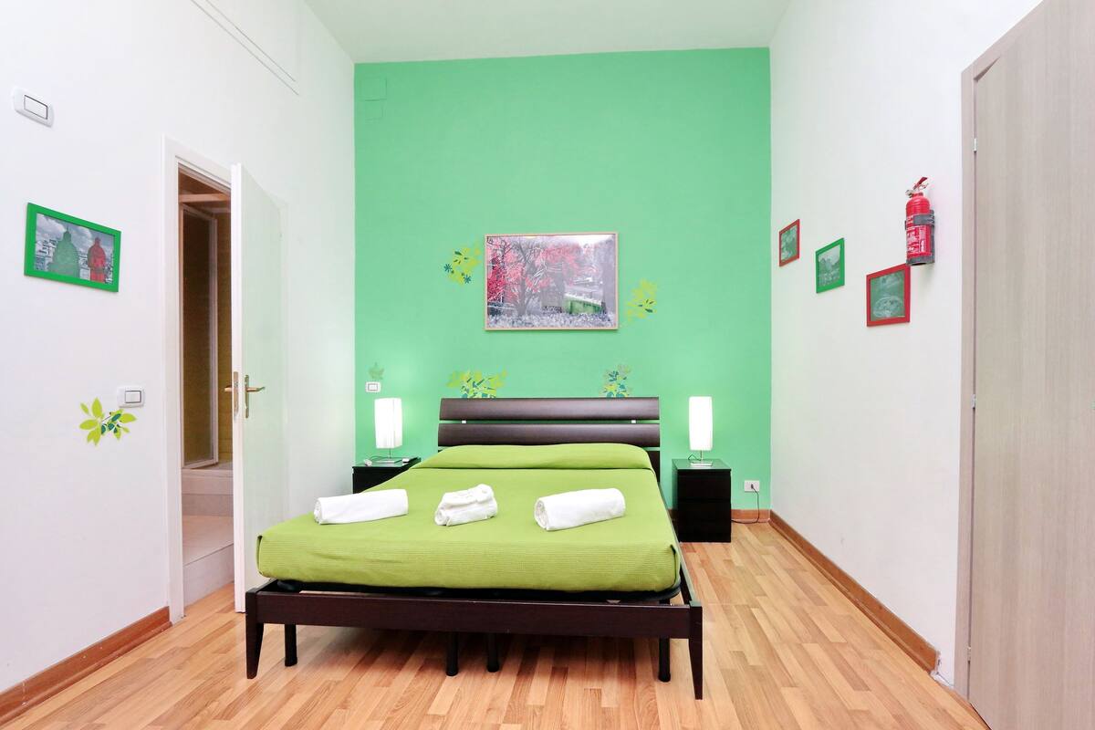 Una stanza con un letto, pareti verdi e una porta che dà su una scala.