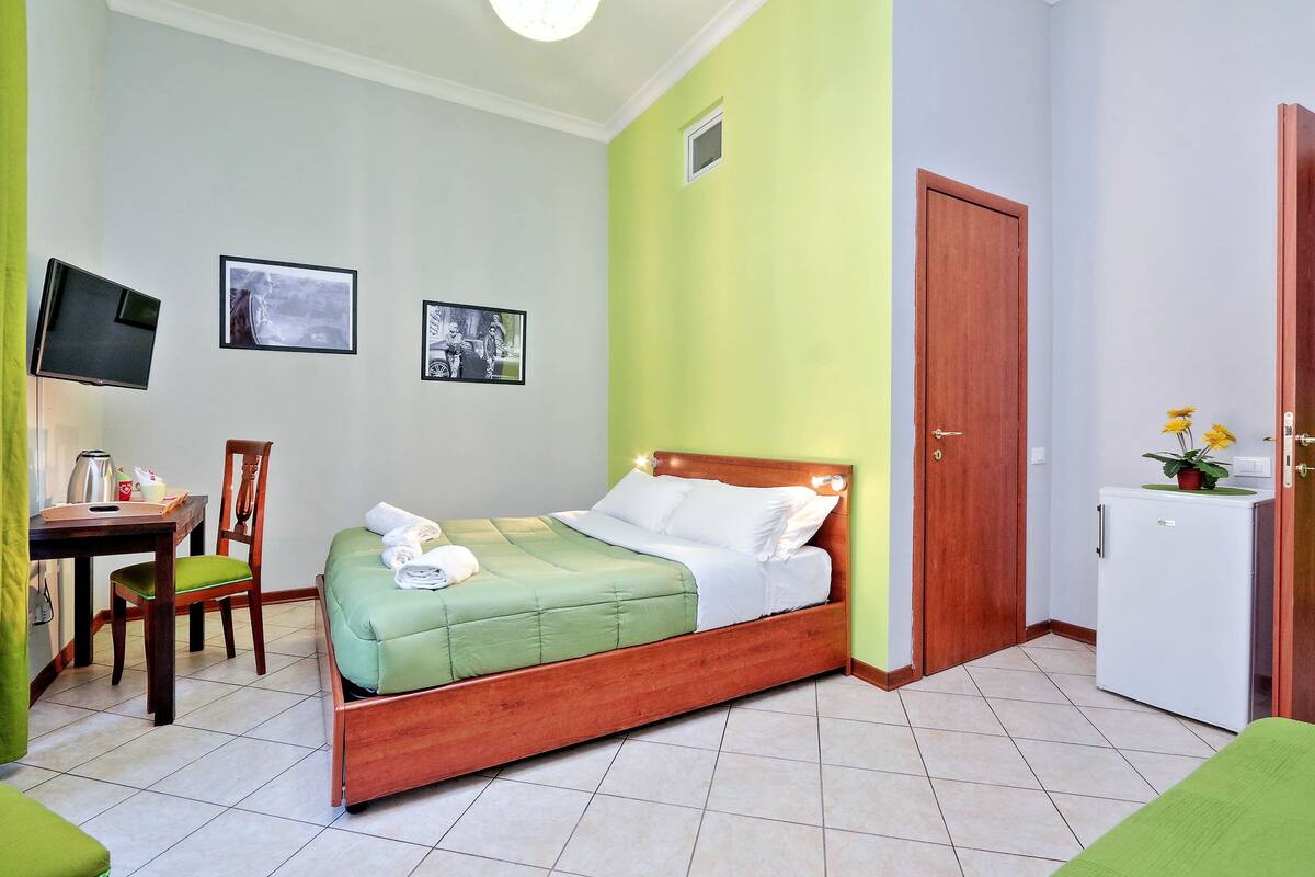 Una camera da letto ordinata con un letto, una scrivania, una sedia, una televisione e un frigorifero.