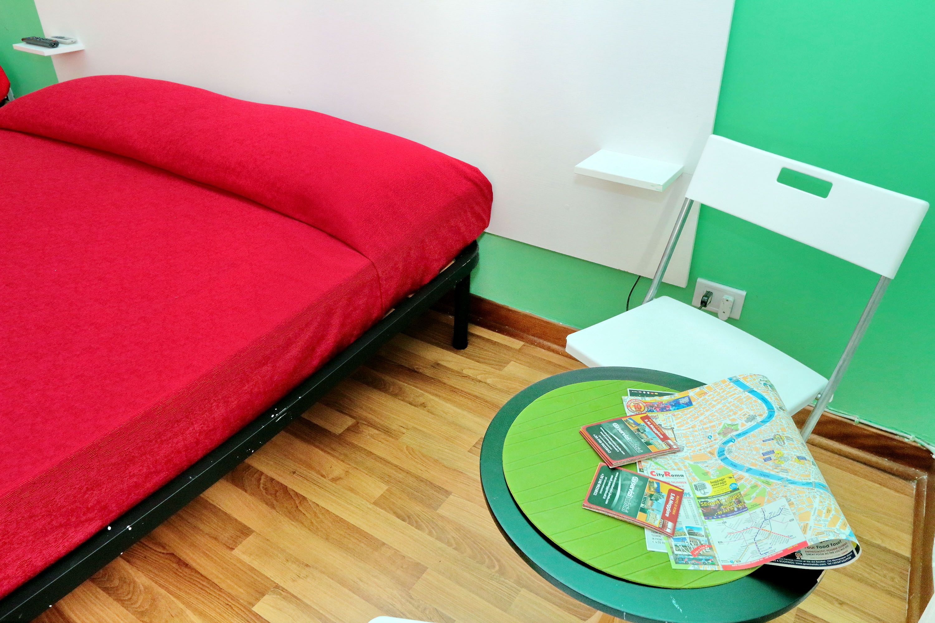 Une pièce avec un lit, une chaise verte, une table avec une carte et une étagère blanche.