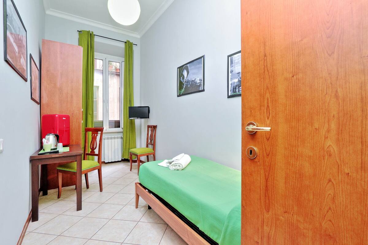Una stanza piccola e ordinata con un letto, una scrivania, una sedia e una televisione.