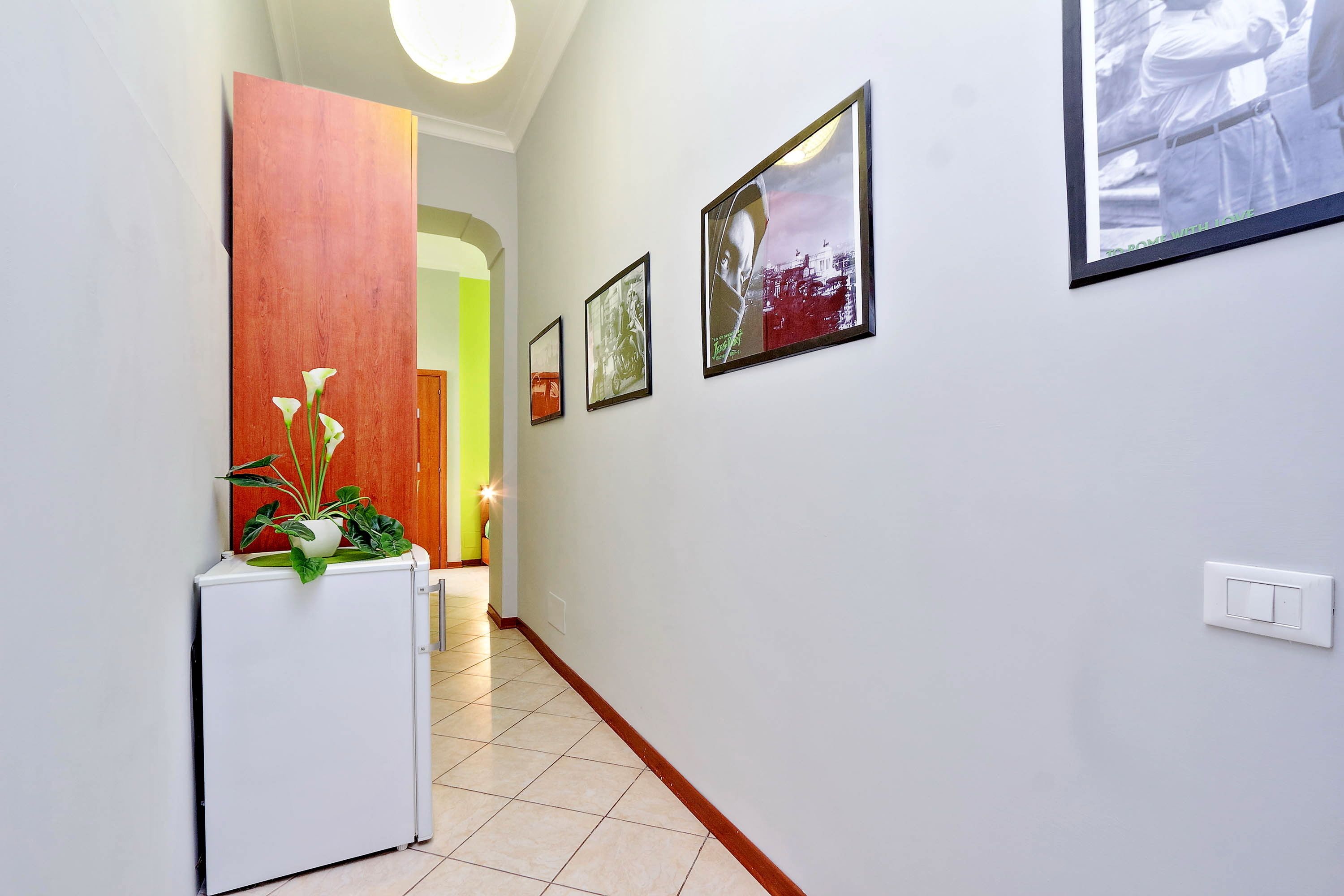 A hallway with a white refrigerator, a wooden panel, and three framed pictures on the wall.